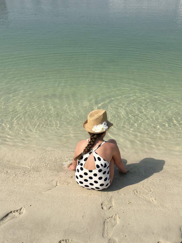 gril sat in polka dot swimsuit and straw hat facing the sea 
