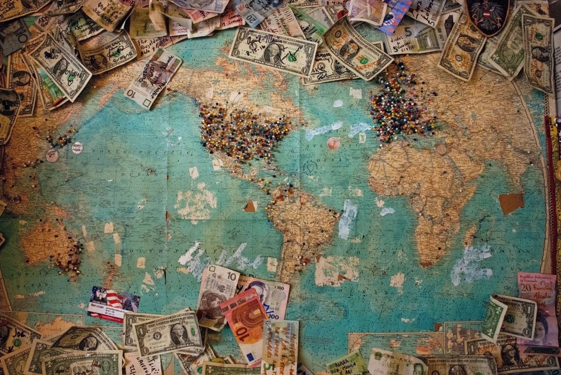 Various currency bills pinned to a large world map with colorful pins in various locations