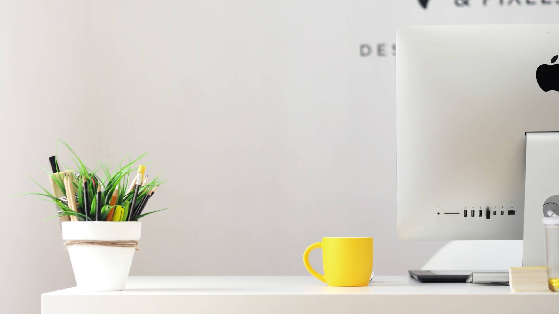 Partial desk photo with mac, yellow mug and plant