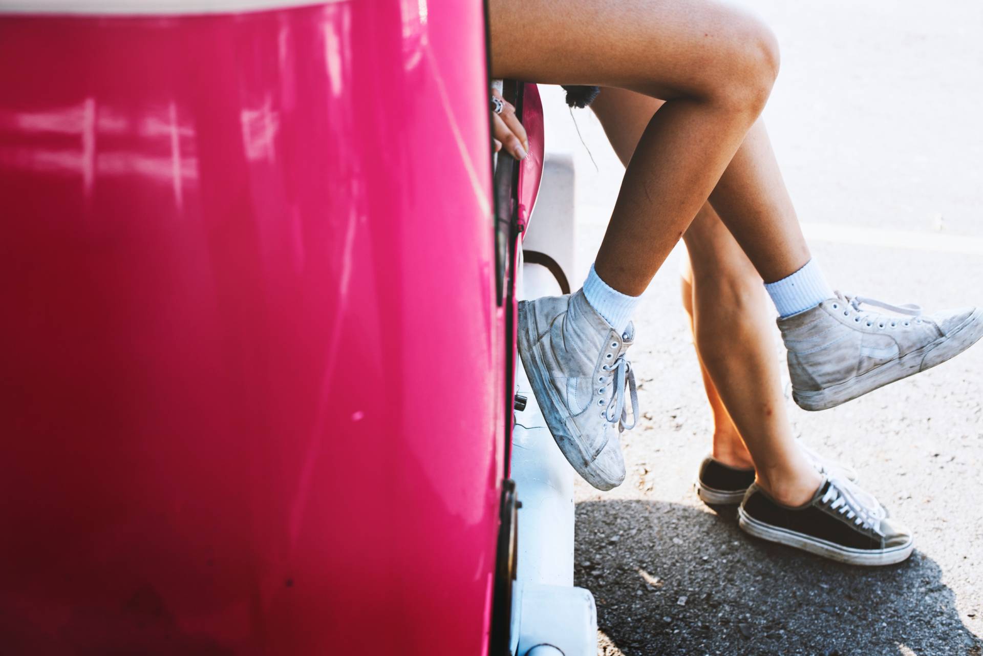 two pairs of girls legs leaning against a pink car
