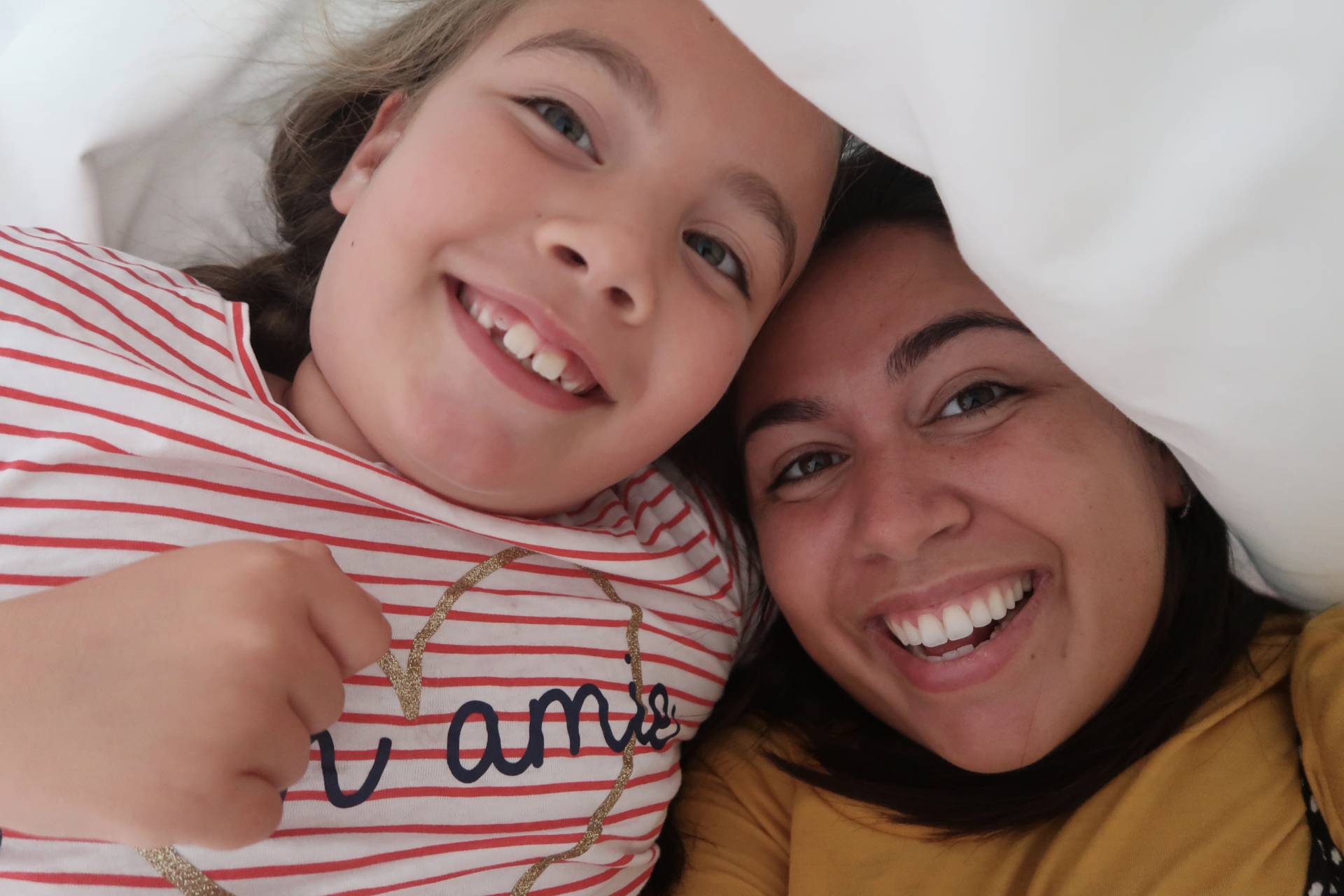 mother and daughter smiling under the bed covers