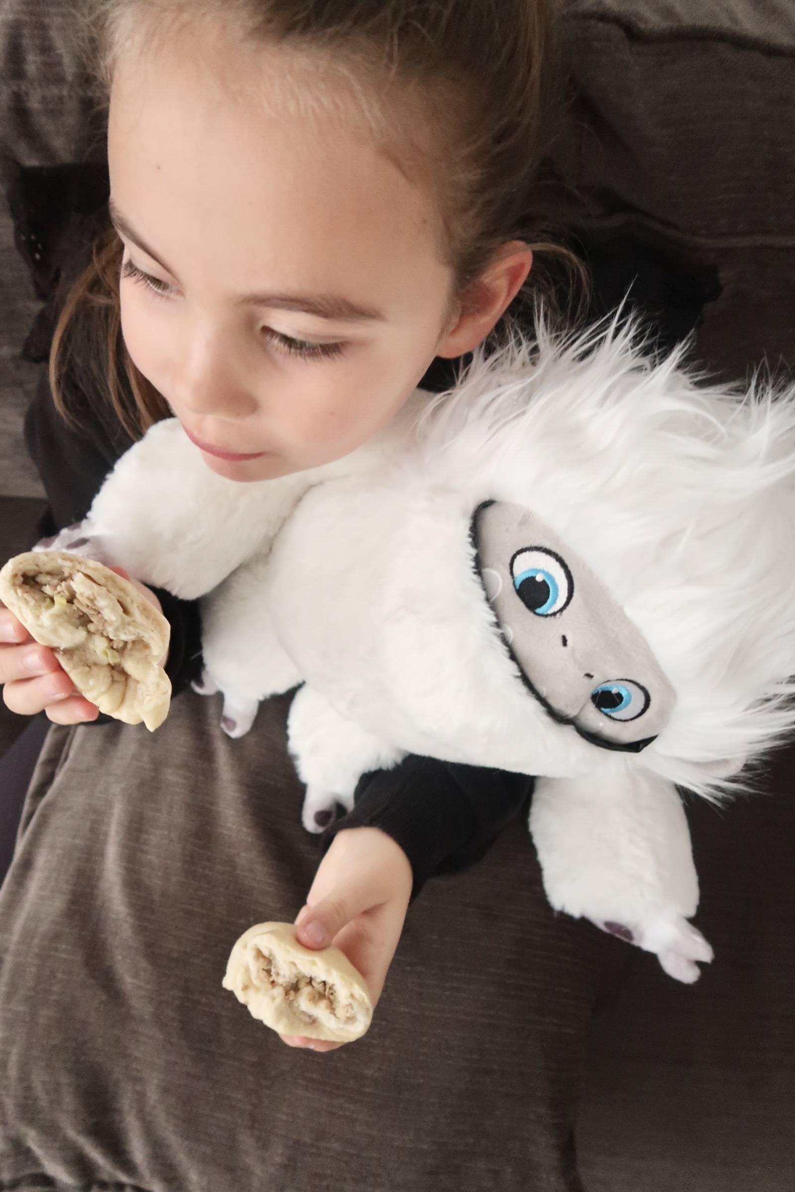 Child eating boo bun while cuddling fluffy yeti toy