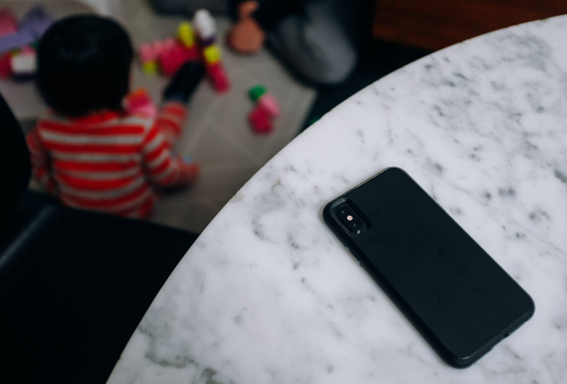 Black mobile phone on marble table with young child playing in background