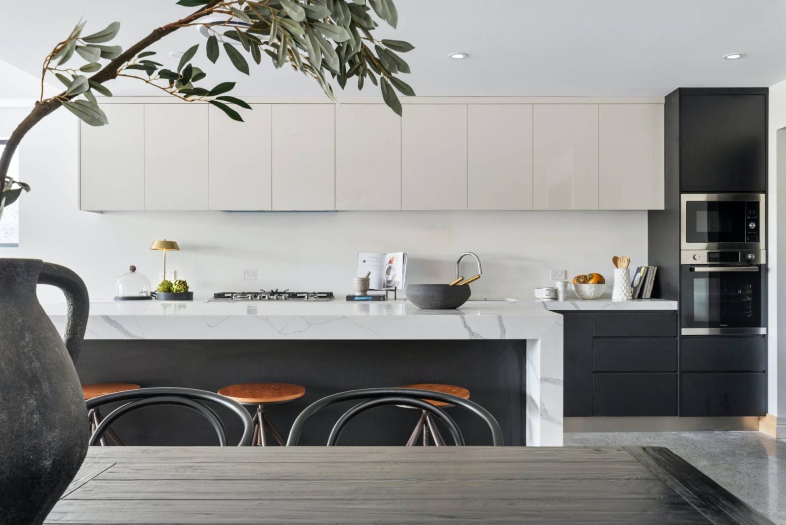 kitchen shot of light wall cabinets and dark grey base cabinets and marble worktops with a dining table in front