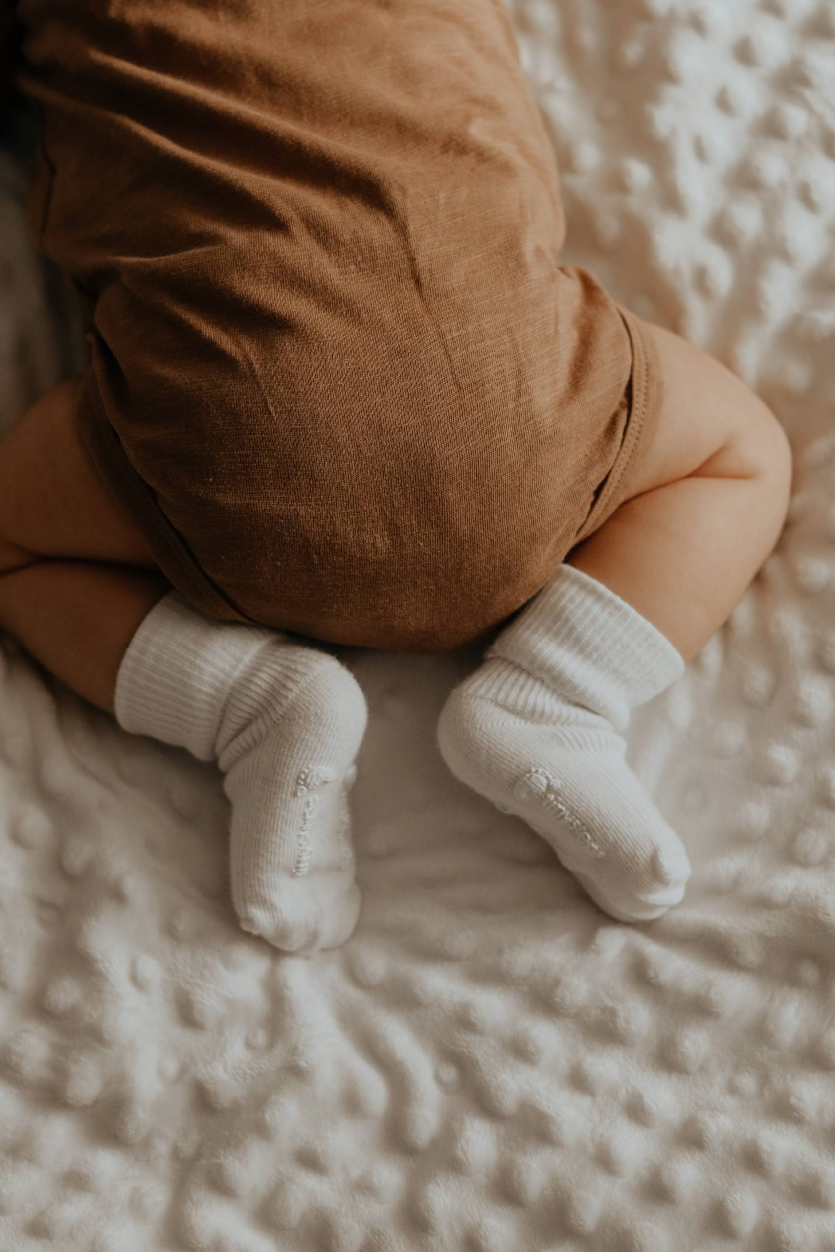 close up shot of newborn baby laid on tummy with legs tucked under wearing white socks and brown babygrow