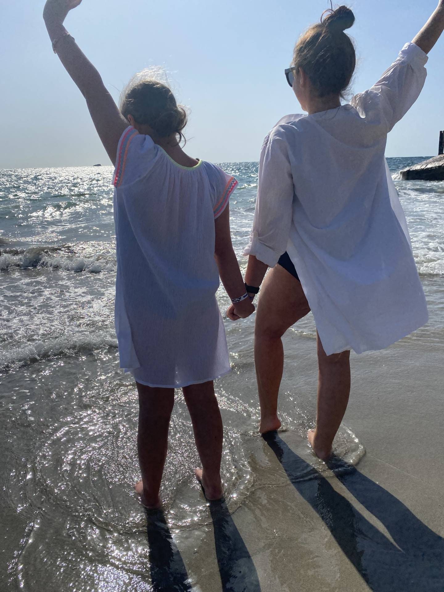 Mother and daughter holding hands looking out to sea with feet in water
