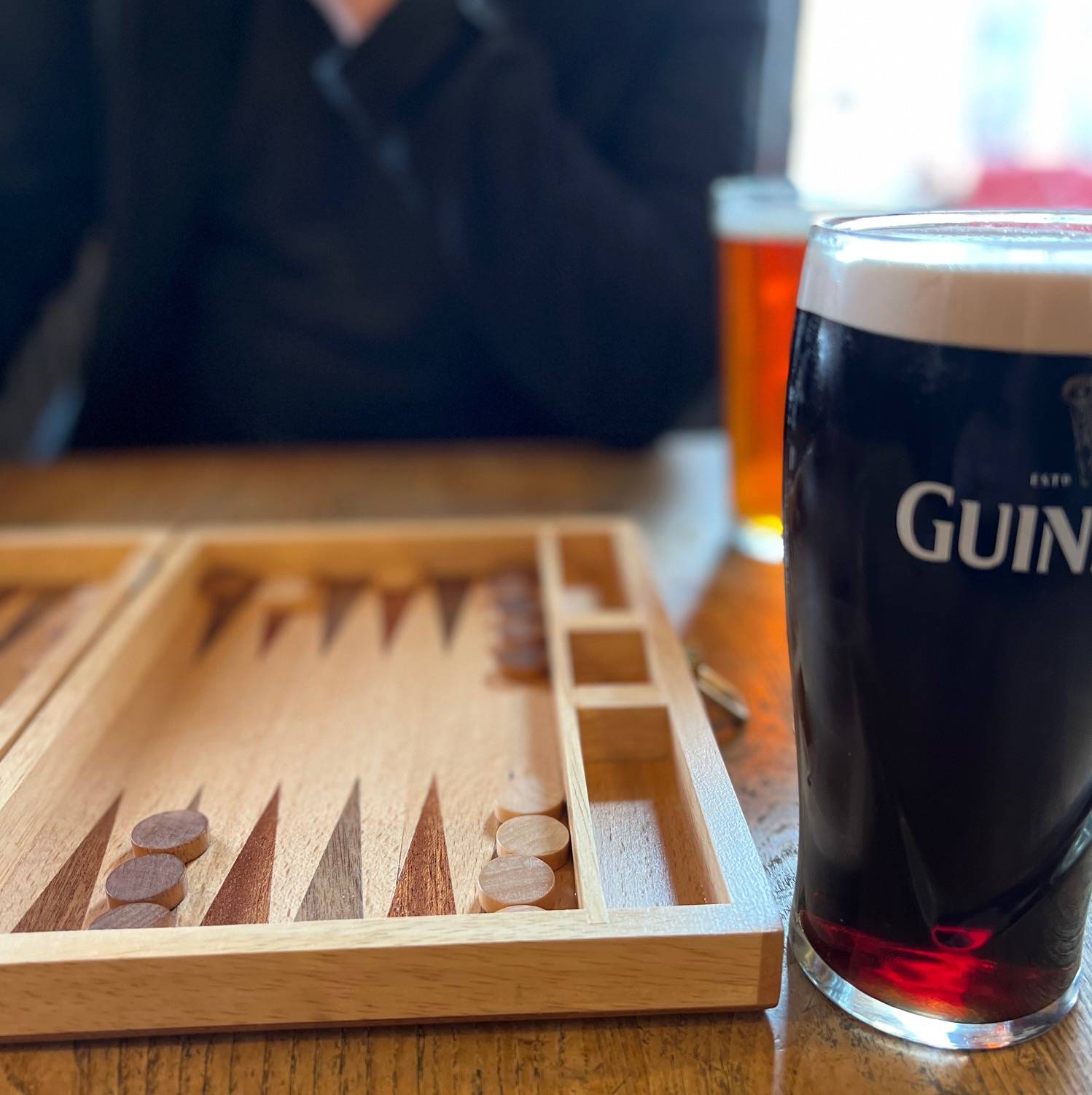 Pint of guinness next to wooden backgammon board in play