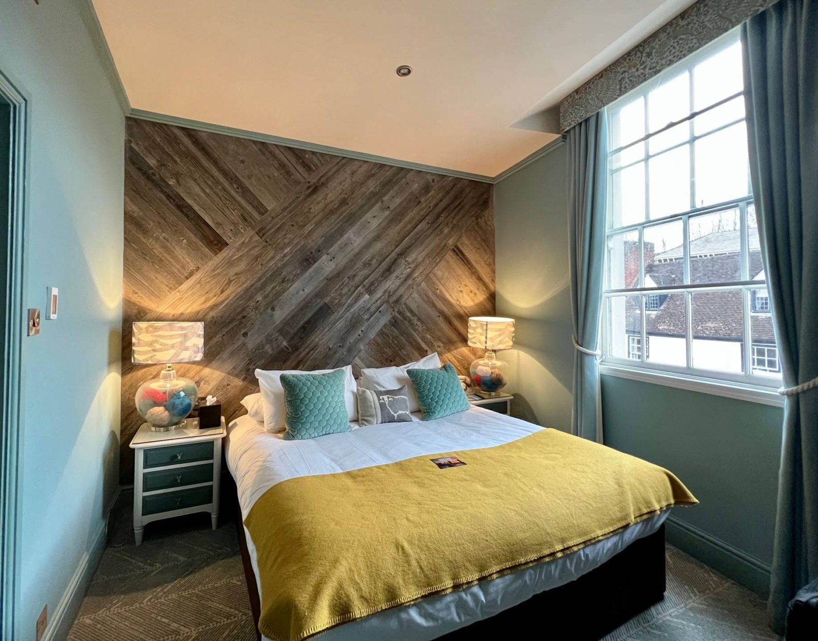 large bed with yellow bedspread in teal room with wooden accent wall