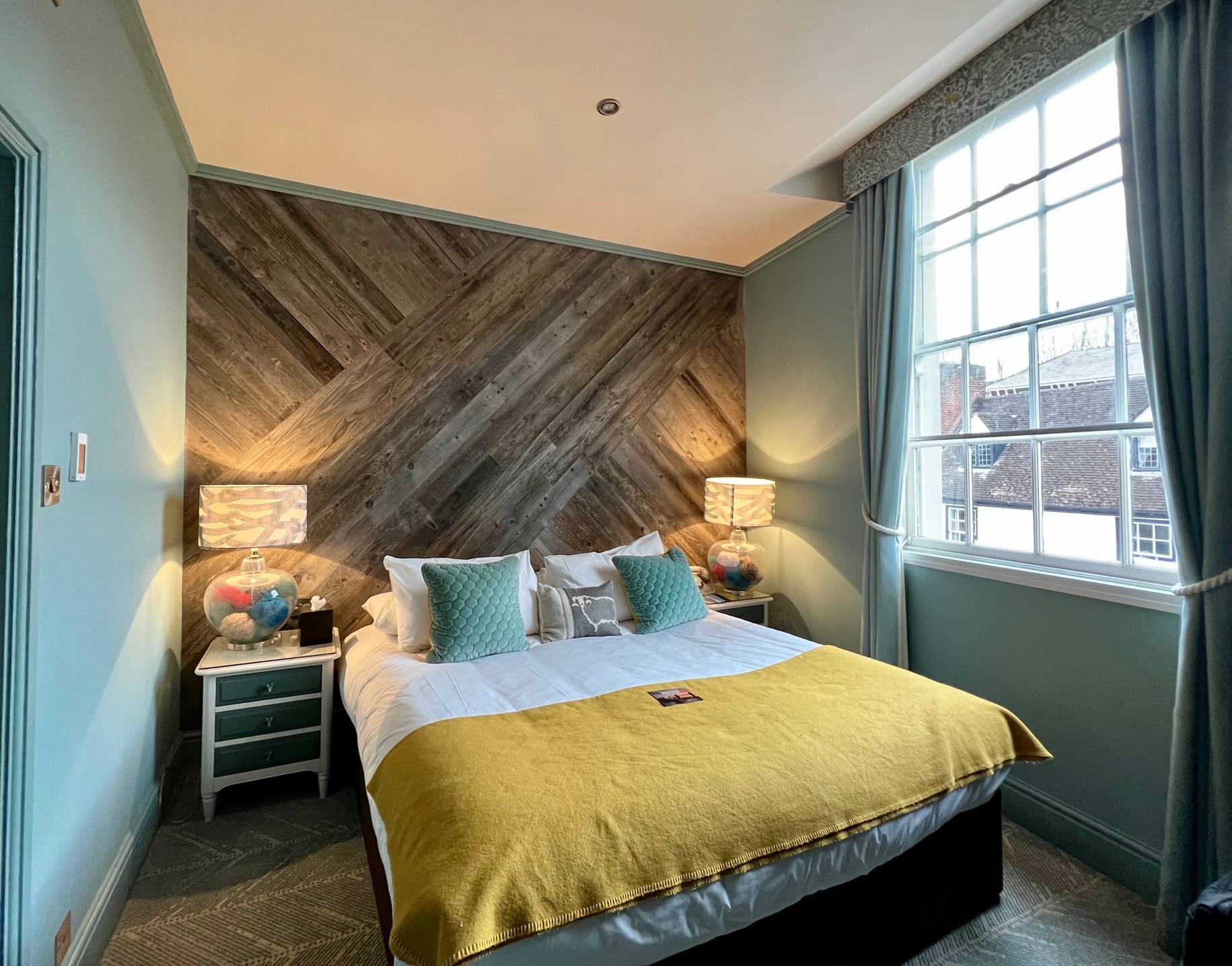 large bed with yellow bedspread in teal room with wooden accent wall