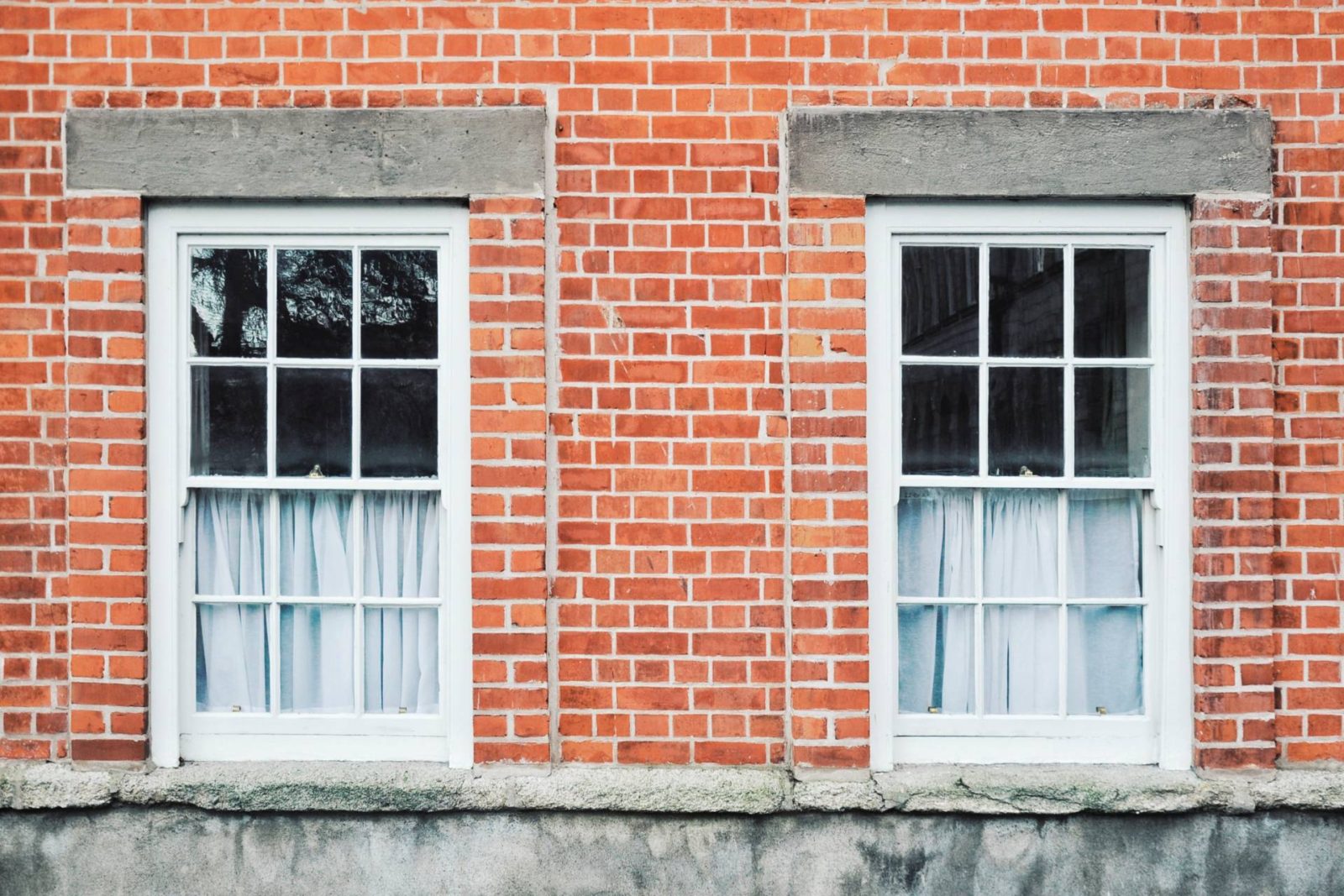 red brick building with two paned sash windows with half net curtains