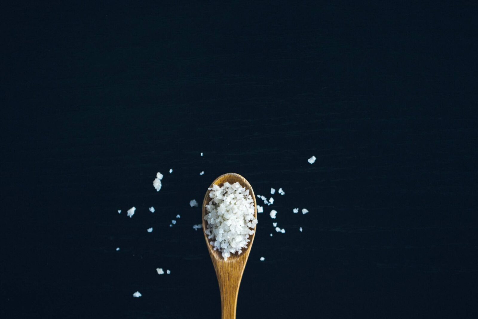 wonden spoon with salt flakes on black background